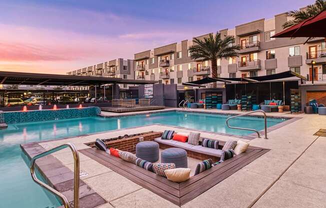 A pool area with a hot tub and lounge chairs in front of a multi-story building.