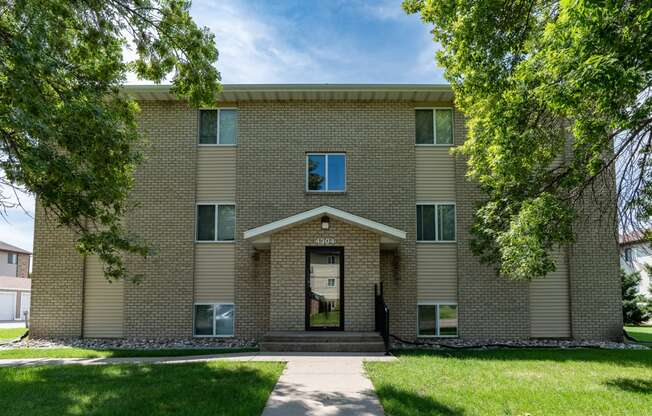 a brick building with a sidewalk in front of it and trees. Fargo, ND Park Circle Apartments.