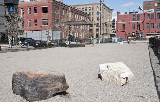 A large rock sits in the middle of a gravel area with a building in the background.