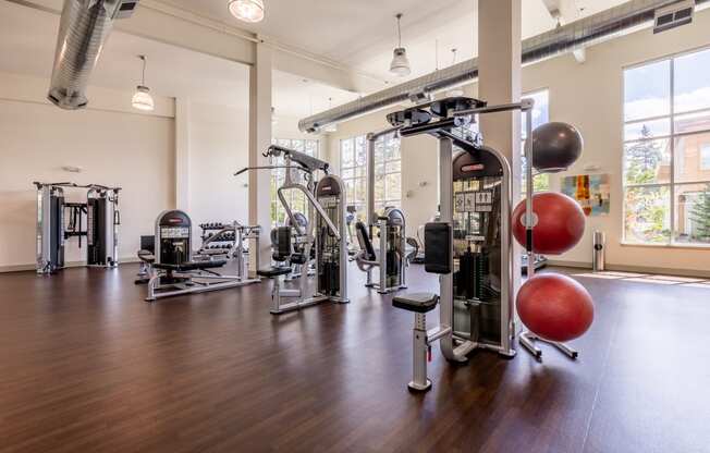 Large open room which is the fitness center with hardwood flooring and many weight systems and inflated work out balls of several sizes.