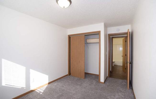 an empty living room with a door to a closet and a hallway to a bathroom. Fargo, ND Country Club Apartments
