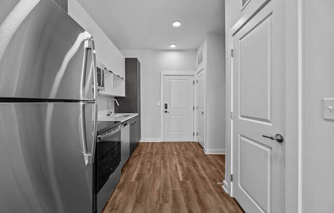 A modern kitchen with a refrigerator on the left and a wooden floor.