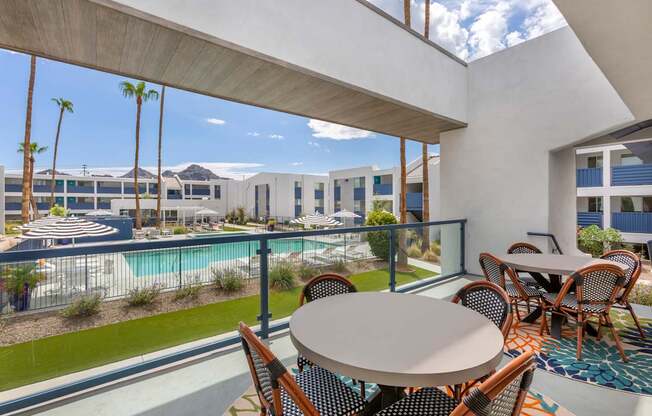 A patio with a table and chairs overlooks a pool and a building.