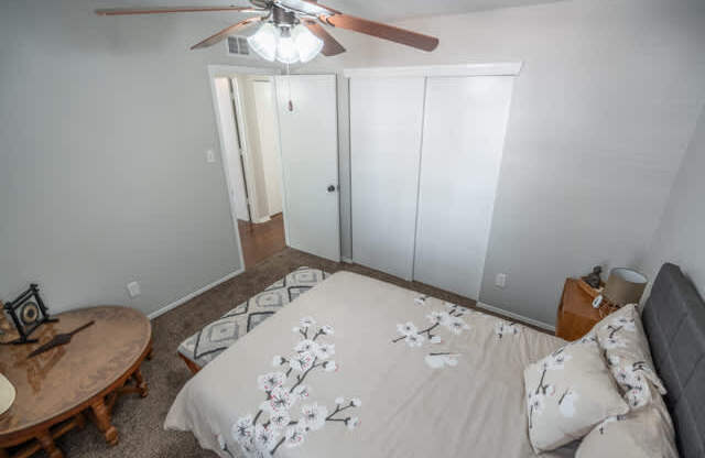 A bedroom with a bed, a ceiling fan, and a small table.