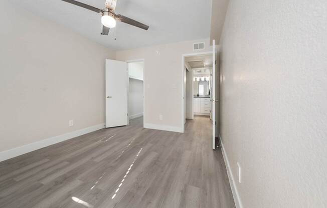 A room with a ceiling fan and light fixture, and a doorway leading to another room.