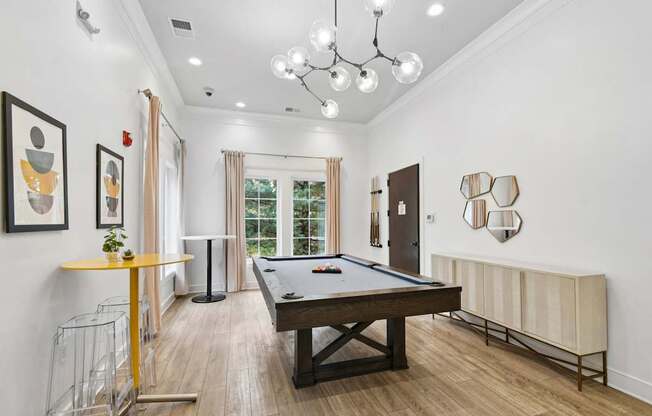 A pool table is in the middle of a room with a yellow table and a chandelier.