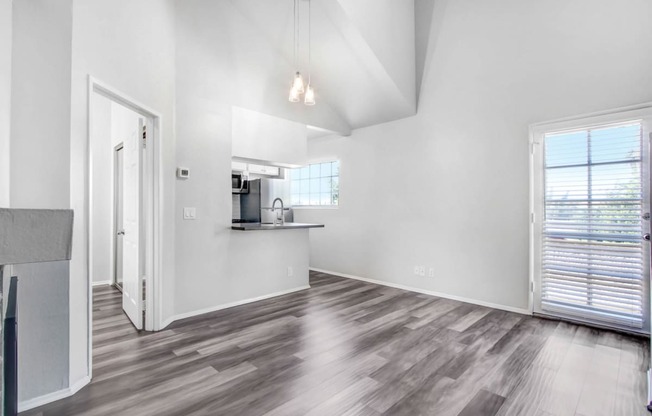 an empty living room with a kitchen and a window