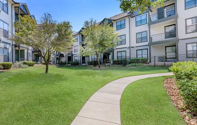 a sidewalk leading to an apartment building with green grass and trees