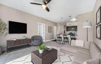 A living room with a grey armchair, sofa, wooden coffee table, and a television on the wall at Copper Creek Apartment Homes, Maize, Kansas