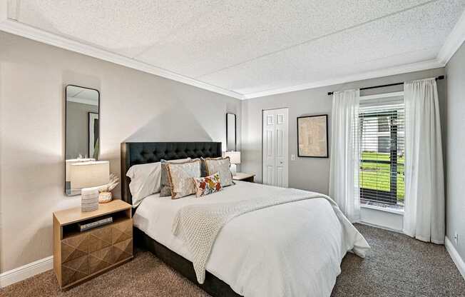 A bedroom with a large bed and a window with white curtains.