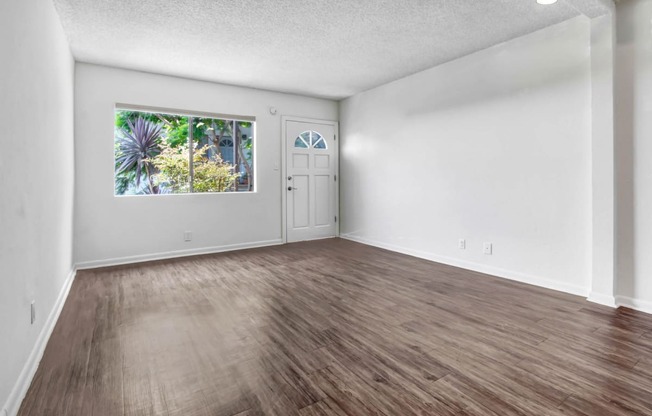 an empty living room with a large window and hardwood floors