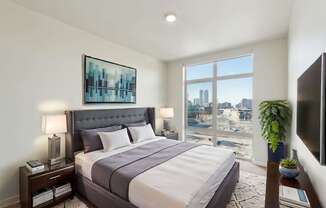A bedroom with a large bed and a city view through the window.