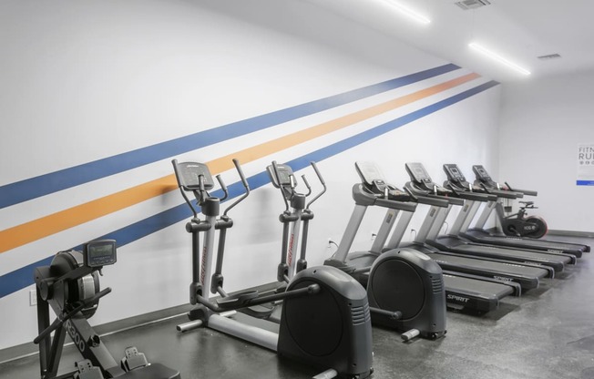 a row of exercise machines in front of a white wall with blue and yellow stripes