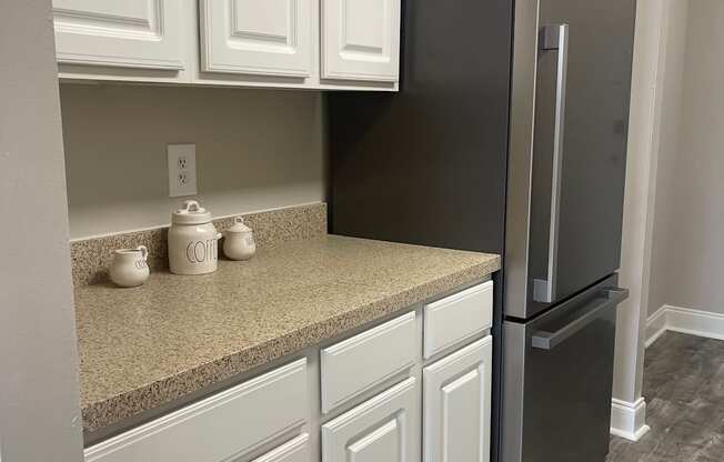 A black fridge in a kitchen with white cabinets.