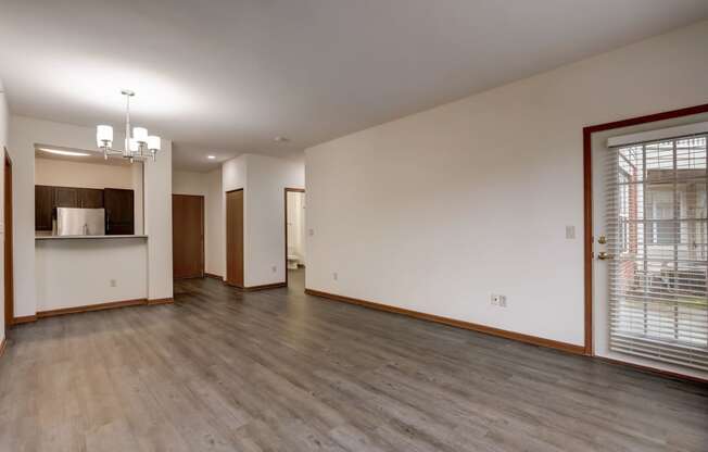 the living room and kitchen of an empty house with wood floors and a large window