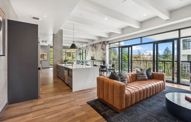 A modern living room with a brown leather sofa and a kitchen in the background.