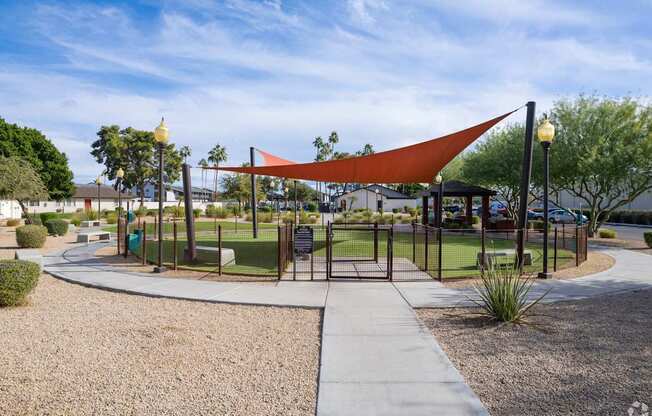 A playground with a red shade structure and a black fence.