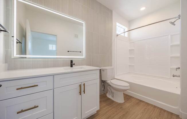 A white bathroom with a large mirror and wooden floors.