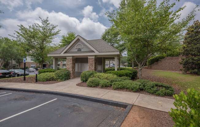 a small brick building with a driveway and trees and bushes