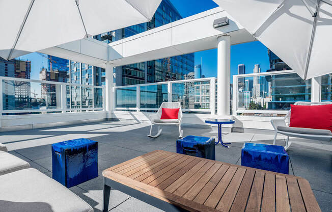 A wooden table is in the middle of a patio with white chairs and umbrellas. at G12 Apartments, Los Angeles, CA