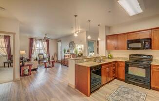 large kitchen with black appliances, dark cabinets, wood style flooring, into open living spaces