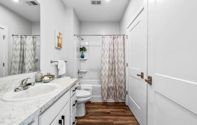 A white bathroom with a marble counter top and a wooden floor.