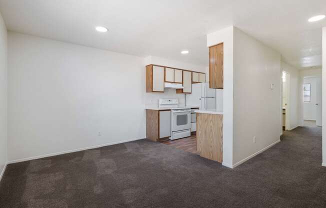 an empty living room and kitchen with white walls and brown carpet