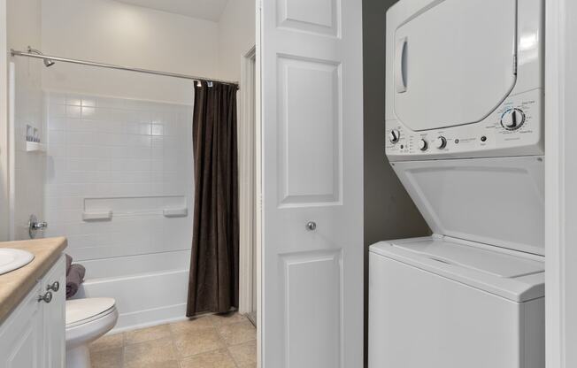 a white washer and dryer in a bathroom with a shower and a toilet