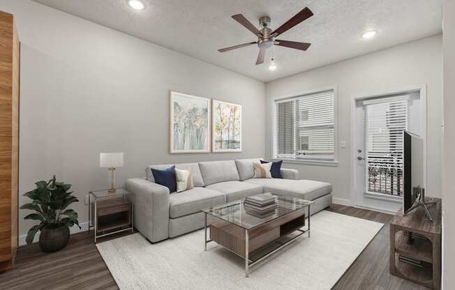 A living room with a grey couch, a glass coffee table, and a ceiling fan.