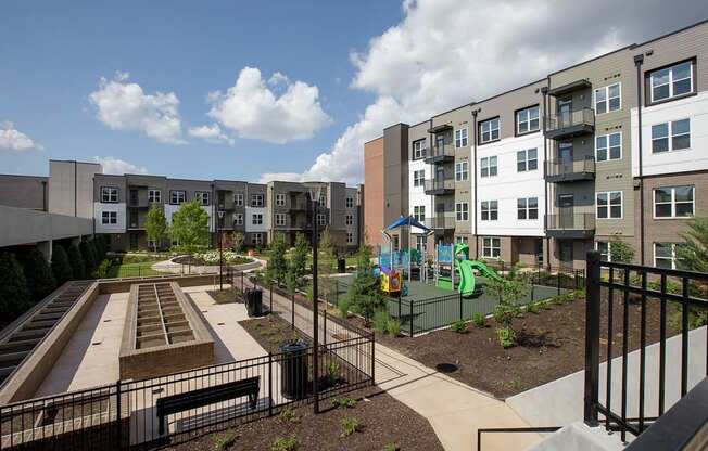 A playground area with a slide and a basketball court is located in front of apartment buildings.