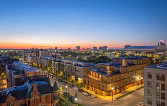 A cityscape at dusk with buildings illuminated and a clear sky.
