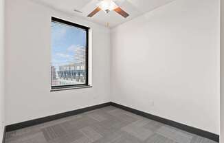 A room with a ceiling fan and a window overlooking a cityscape.