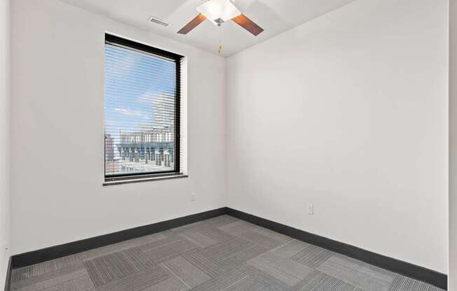 A room with a ceiling fan and a window overlooking a cityscape.