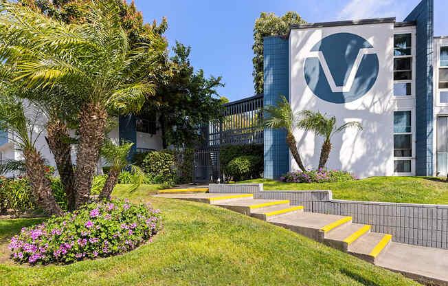 A building with a logo on it is surrounded by a green lawn and trees.