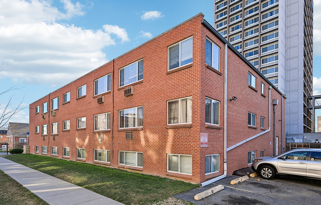 Charming red-brick apartment building with modern windows, nestled in a bustling urban setting, offering convenient parking and a vibrant community atmosphere.