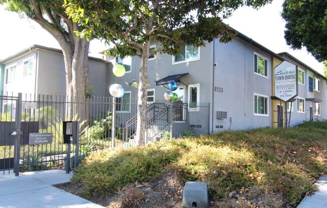 a gray building with a black fence and a tree in front of it