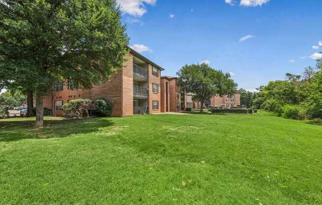 A grassy area in front of a brick building with trees.