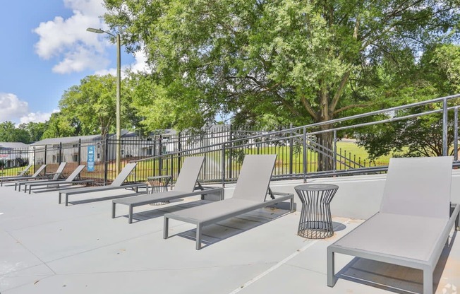 a row of white chaise lounge chairs sit on a concrete patio with trees in the background