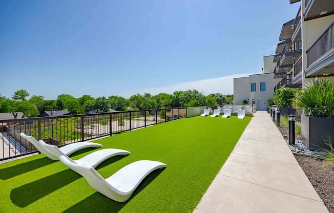A row of white chairs are lined up on a green lawn.
