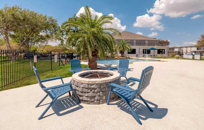 A fire pit surrounded by blue chairs in a sunny outdoor setting.