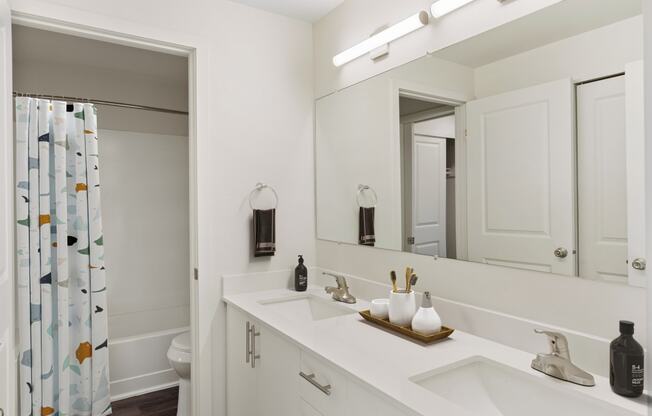 Full bathroom with a double sink vanity and cabinet storage, a large mirror, and a door to the shower and toilet.