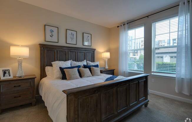 A bedroom with a large bed, two lamps, and pictures on the wall.