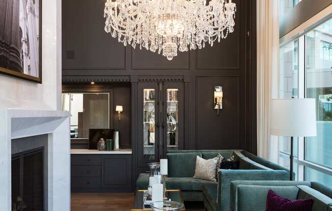 a large chandelier hangs above a large living room with green couches and a large