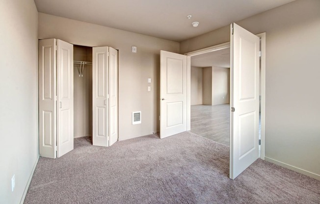 A room with a carpeted floor and white walls with a few open doors.