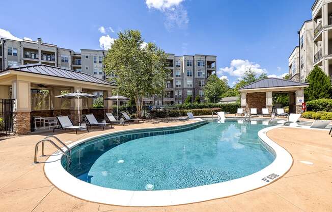 A large swimming pool surrounded by lounge chairs and umbrellas in a sunny day.