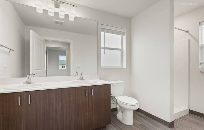 A white bathroom with a wooden vanity and a white toilet.