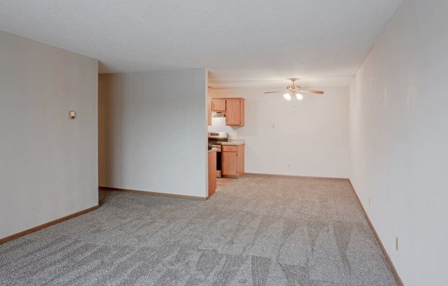 an empty living room with a ceiling fan and a kitchen