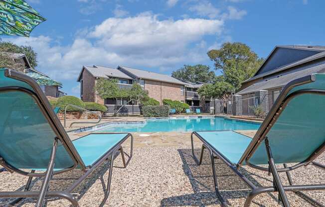 Blue lounge chairs by the pool with apartments in the background at The Pearl apartments in Shreveport, LA
