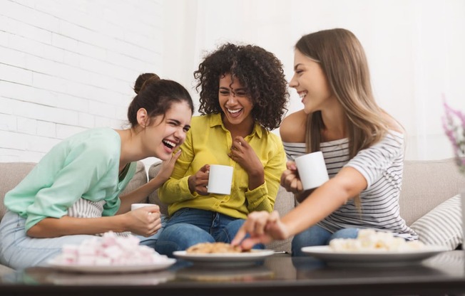 a group of women sitting on a couch eating food and drinking coffee