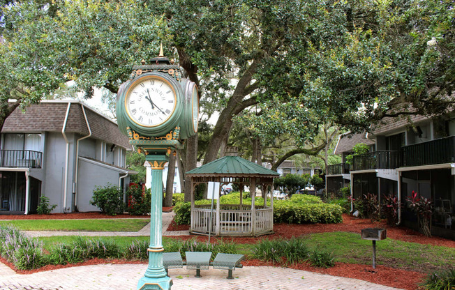 a clock in the middle of a park with a gazebo